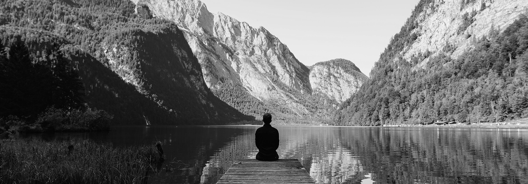 a man meditating on the end of a dock in front of a lake in the mountains